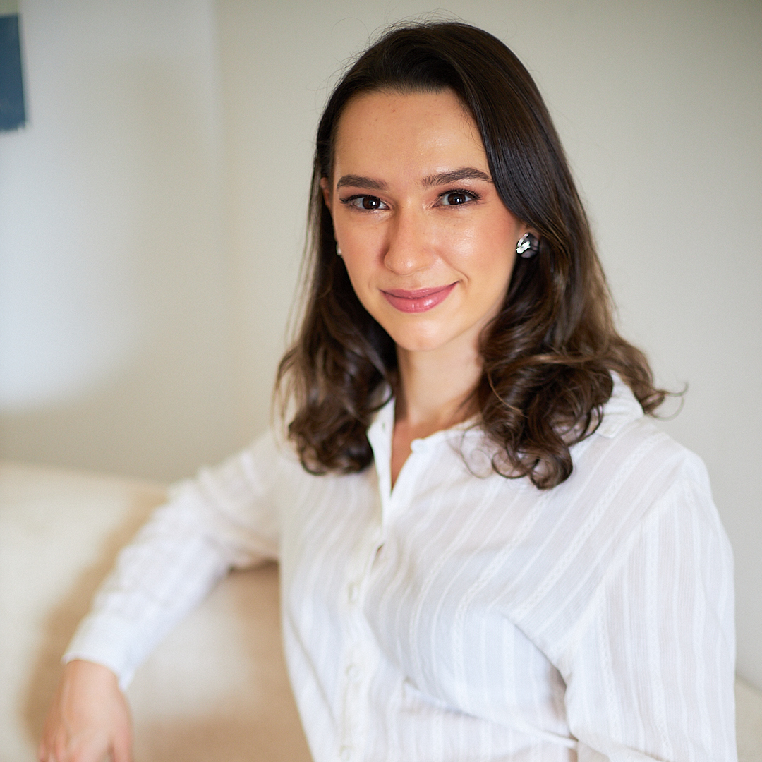 Dra. Lívia Macedo sentada em sofá claro, usando camisa branca
