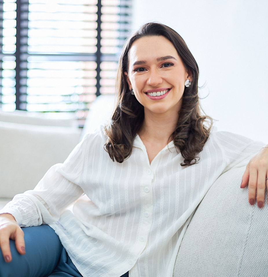 Dra. Lívia Macedo sentada em sofá claro, usando camisa branca